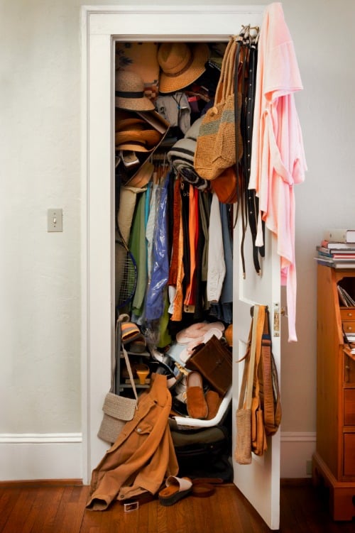 Messy closet in bedroom overstuffed with clothes, hats, woman's apperal.