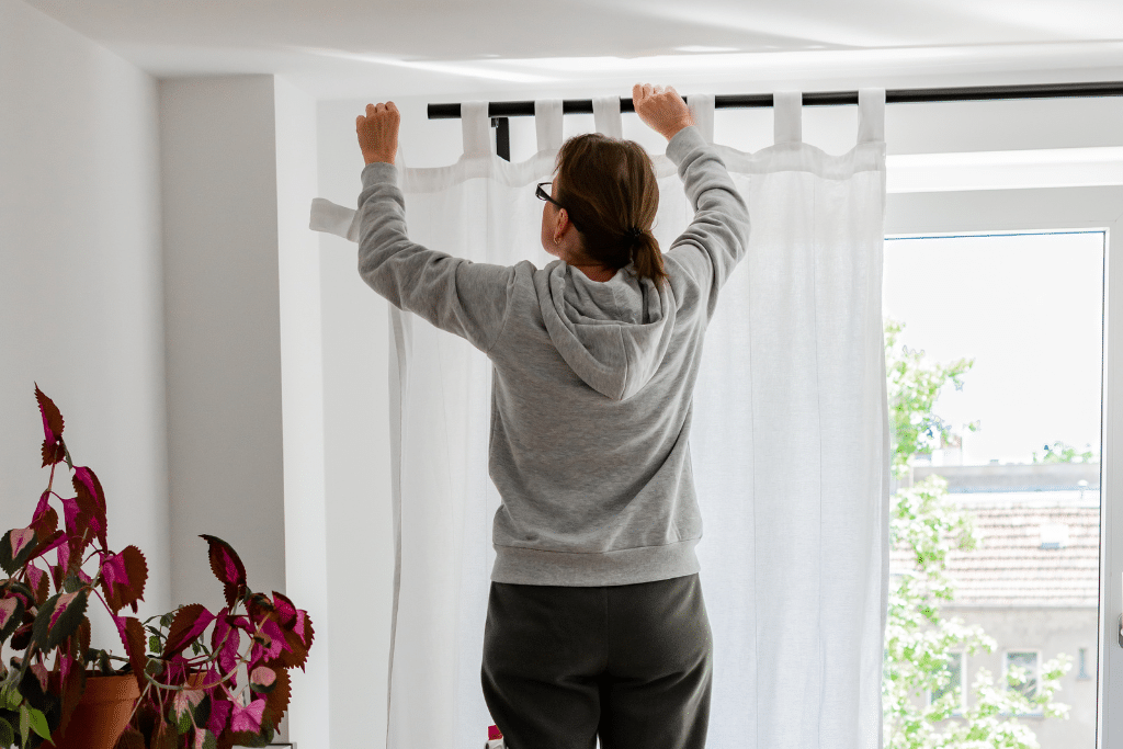 woman adding white linen curtain to black curtain rod