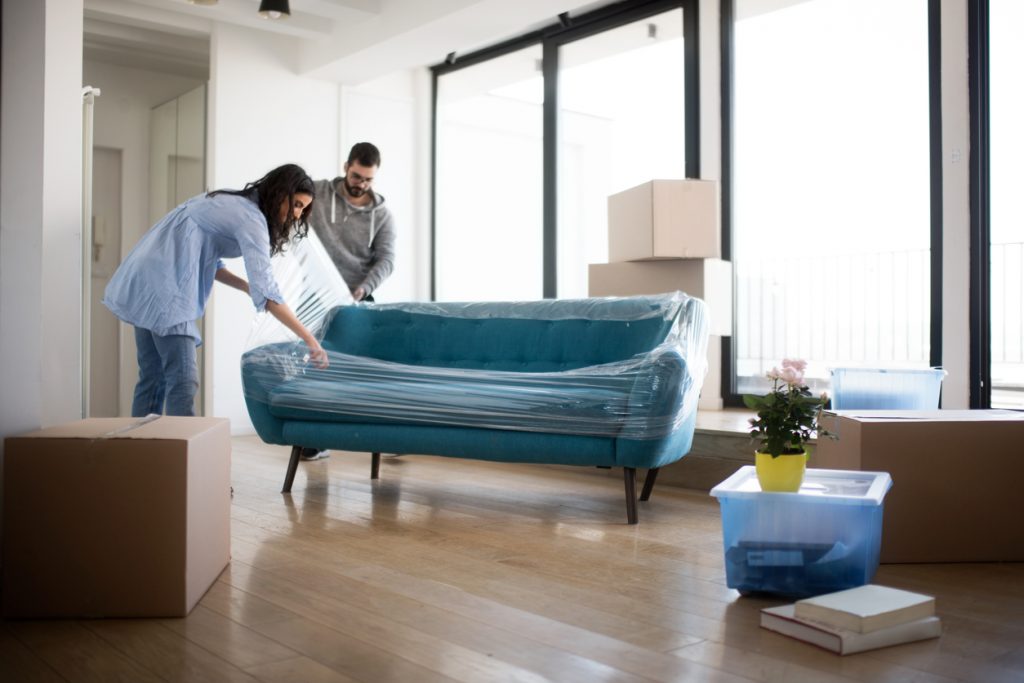 Young couple moving out of the apartment and wrapping up the sofa.