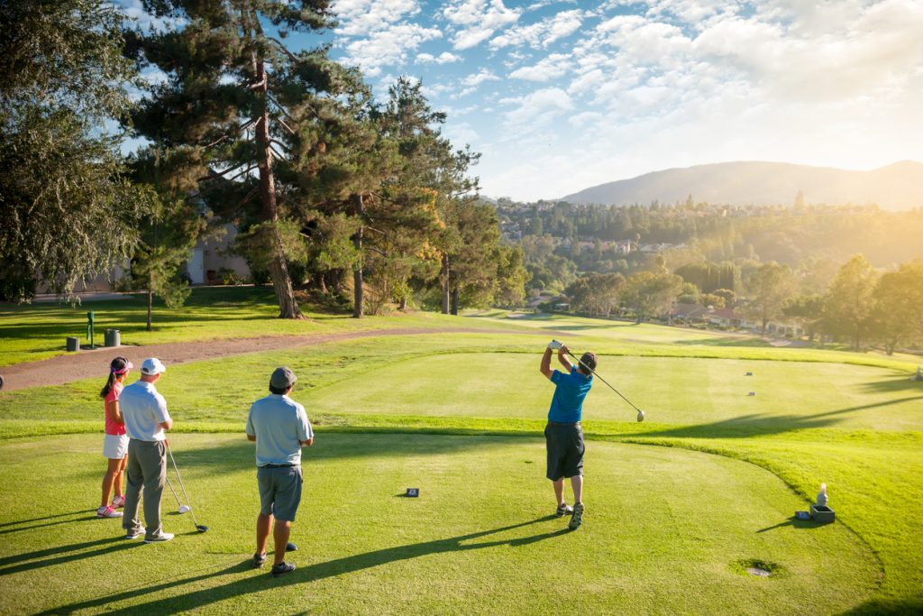 A man teeing off as his friends watch him hit on a beautiful day at the golf course. 