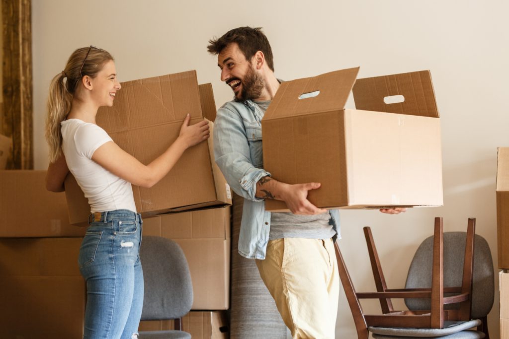 Young couple carrying big cardboard box out of home. Moving items to storage.