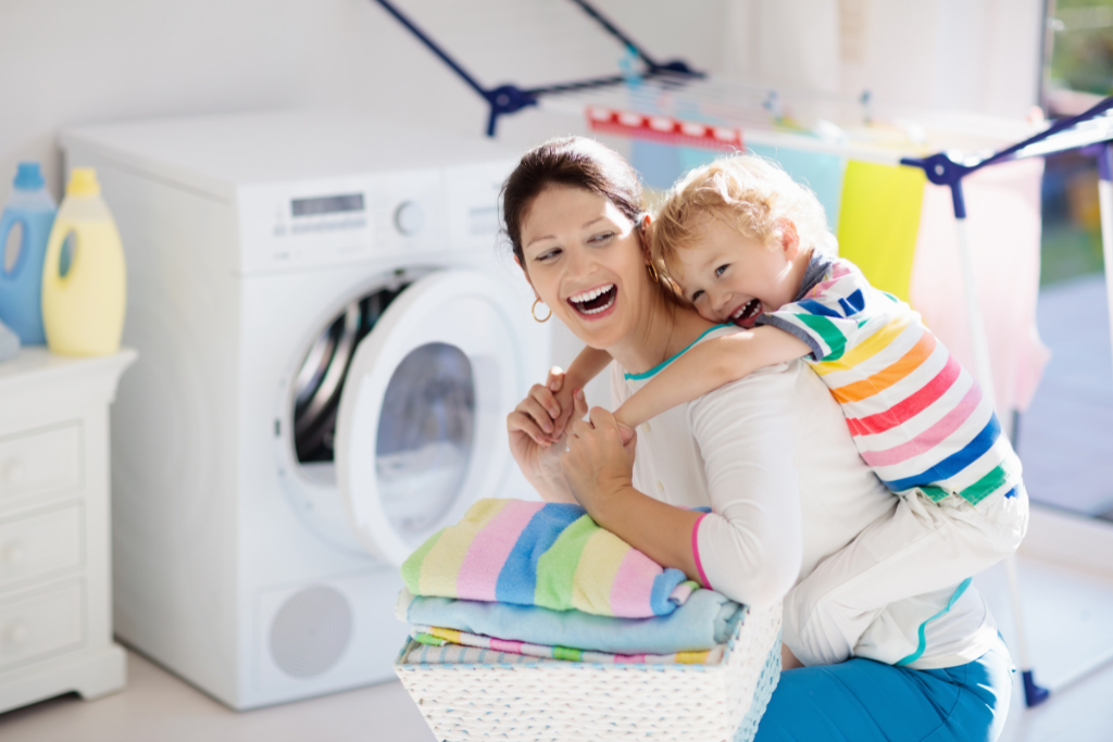 Mom and son laughing near washing machine. Storage Newbury Park experts recommend maintaining a clean washer for a longer life span.